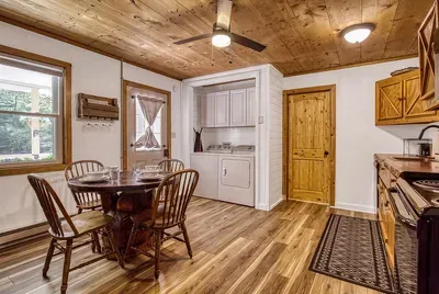 Everything within a few steps — table, kitchen, laundry behind the door. Small cabin, full setup, nothing you'd have to drive into town for mid-stay.
