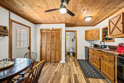 Dining table under a pine ceiling, doors open to the porch and the green beyond. Long breakfasts, longer card games — this table earns its keep.