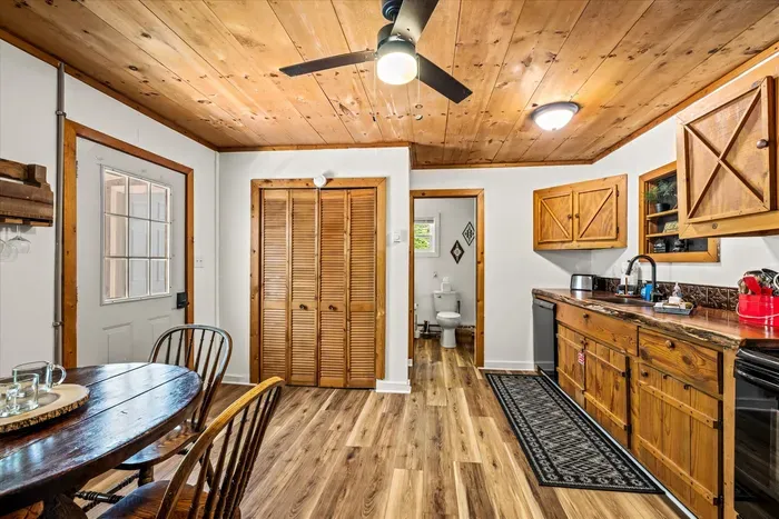 Dining table under a pine ceiling, doors open to the porch and the green beyond. Long breakfasts, longer card games — this table earns its keep.