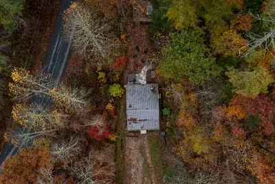 Fall from above — one cabin, one gravel drive, and a whole hillside turning gold and rust. Leaf season books out early up here for a reason.