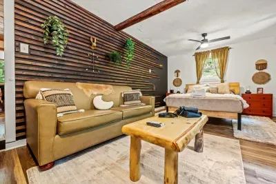 Bed and lounge in one tucked-away room — sofa, log bench table, and light coming in from two sides. The spot everyone quietly hopes they get assigned.