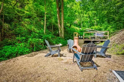 Fire circle ringed in Adirondack chairs with the ridge rising green behind. Firewood's stacked, the chiminea's ready — evenings here run long by design.