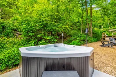 Private hot tub under a full canopy of green, jets running, steam rising into cool mountain air. Soak after the hike or before breakfast — nobody's counting.