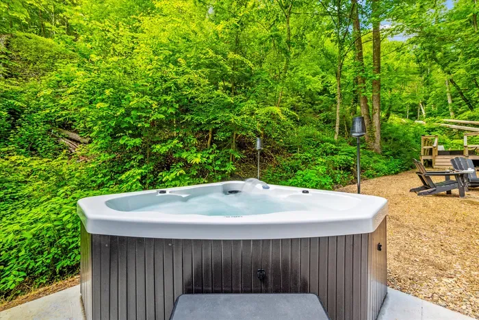 Private hot tub under a full canopy of green, jets running, steam rising into cool mountain air. Soak after the hike or before breakfast — nobody's counting.
