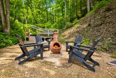 Chiminea fire circle with Adirondack chairs pulled close and forest climbing the ridge behind. Firewood, marshmallows, and a night sky that shows up in full out here.