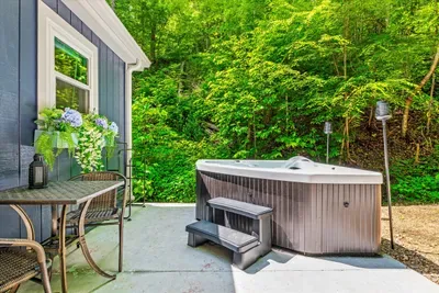 Hot tub just off the cabin with a bistro table alongside — bring the drinks out and stay. Hydrangeas, tiki torch lit, forest on all sides, no neighbors to wave at.