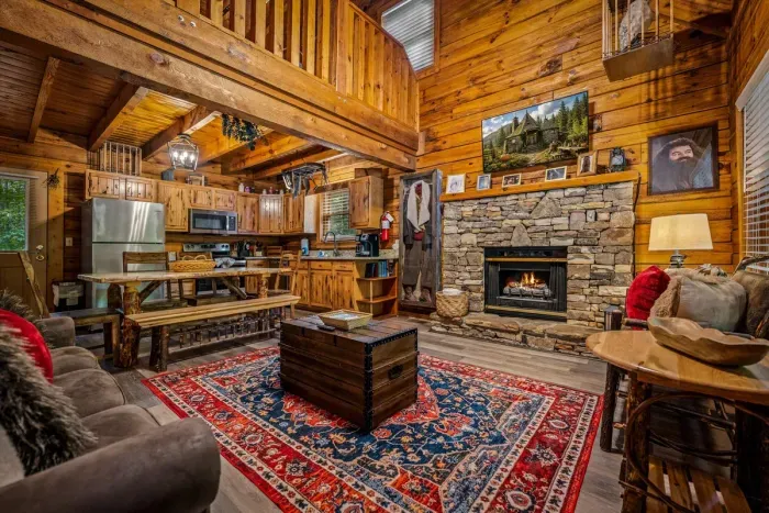 Vaulted log great room anchored by a floor-to-ceiling stone fireplace and a smart TV — sink into the sectional, feet up, mountain quiet on the other side of every window.