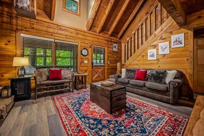 Open-concept living with leather seating, wood-beamed loft above, and light pouring in through the trees. Room enough for everyone, corners enough for anyone who wants their own.