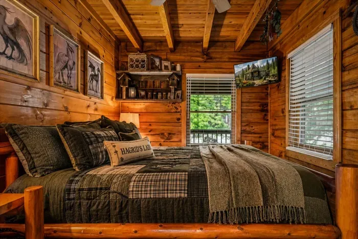 A handcrafted log bed dressed in flannel plaid, with windows opening straight onto green — sleep with one cracked and wake to birdsong instead of an alarm.
