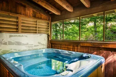 Jets running, water blue, forest pressing right up to the windows — the hot tub is screened, private, and open in all four seasons. First one in claims the best seat.