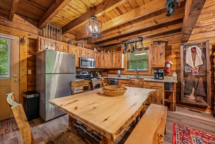 A handcrafted pine table sits beside the full kitchen — stainless appliances, room to prep, and a fireplace glowing just past the counter. Cook in, stay in, linger long.