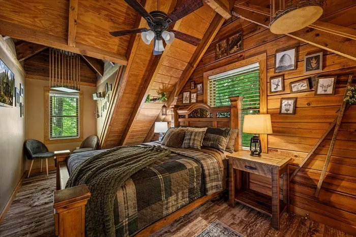 A loft bedroom tucked beneath the A-frame beams — gallery wall, treetop window, and the kind of hush you only find one floor above everyone else in the cabin.
