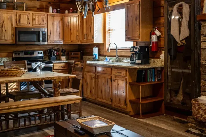 Coffee bar, full-size range, deep sink, and a window looking straight into the woods — mornings start right here, mug in hand, long before the rest of the cabin stirs.