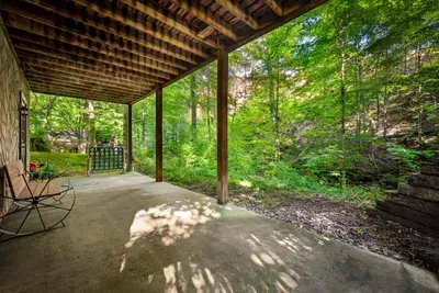 A covered lower patio with rockers facing straight into the woods — shade on hot afternoons, dry seats in a mountain rain, and green as far as you can see from here.