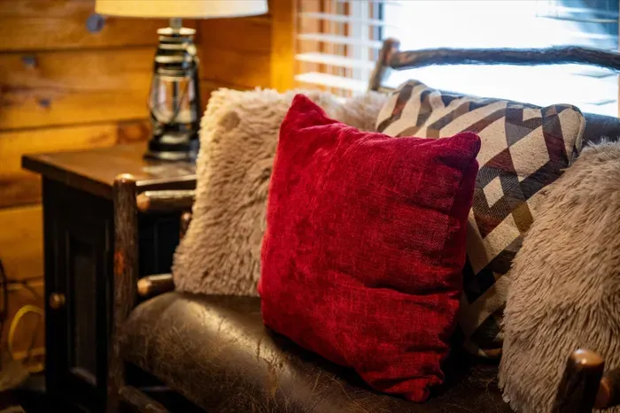 Faux-fur throws, a crimson pillow, and a lantern glowing on the side table — this is the reading chair guests quietly compete for once the fire gets going.
