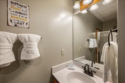 Hand-lettered signage, plush white towels, and a robe waiting on the hook — even the bathrooms here carry the cabin's story. Small touches, noticed on every single stay.
