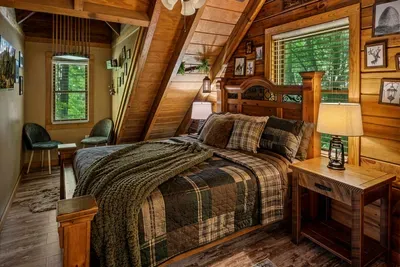 A private loft retreat with a plaid-quilted bed, lantern lamp, and a chair angled toward the window. Read until the woods go dark and the crickets take over the soundtrack.