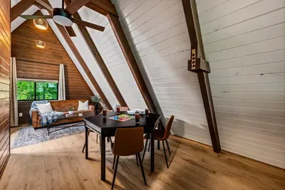 Loft lounge framed by soaring A-frame beams — a quiet perch for coffee or a game with the Smoky Mountain treetops right in the window. Guests' favorite hideaway up top.