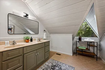 Loft-level vanity tucked beneath the A-frame slope, with a triangle window peeking into the canopy. Even the bathrooms here have a view worth pausing for.