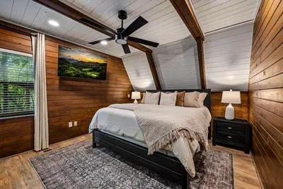 A-frame bedroom with a sloped wood ceiling, smart TV, and window to the green. Character in every beam and a bed you'll be glad to come home to each night.