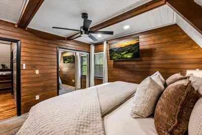 Wood-wrapped bedroom that opens through glass doors toward the trees — smart TV, plush bedding, and morning light spilling in. Private, bright, and built to linger.