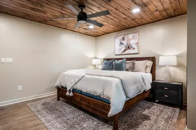 Restful queen room under a warm wood-plank ceiling — crisp linens, soft lighting, and mountain quiet that makes lights-out effortless. Wake up ready for whatever's next.