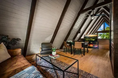 Loft lounge framed by soaring A-frame beams — a quiet perch for coffee or a game with the Smoky Mountain treetops right in the window. Guests' favorite hideaway up top.
