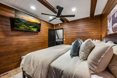 Snug wood-lined bedroom with a smart TV and layered linens made for slow mornings. Pull the covers up, cue a show, and let the mountain quiet do its thing.