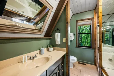 Ensuite bath wrapped in forest green, with a vanity and A-frame window pulling the trees right inside. Everyday routines feel a little more like a getaway up here.
