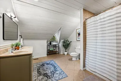 Bright loft bath with a shower-tub combo under the A-frame ceiling — clean, roomy, and just right for a house full of guests. Function meets a little cabin charm.