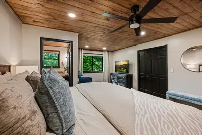 Sage-toned bedroom under a warm wood ceiling with its own TV and a window to the canopy. Soft, calm, and yours for the week — the room you won't want to leave in the morning.