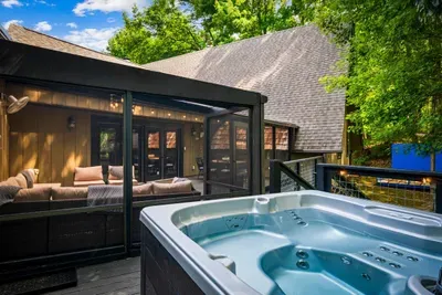 Private hot tub and screened porch tucked into the treeline — soak, lounge, repeat. The outdoor setup that makes leaving the cabin optional.
