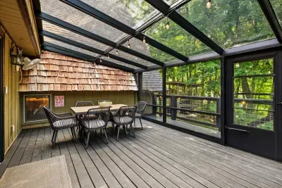 Screened-in deck with a dining table wrapped in treetops — bug-free meals, fresh air, and forest on all sides. Breakfast out here beats any indoor table.