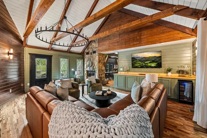 Open-concept great room flowing into a wet bar — vaulted beams, stone accents, and buttery leather couches under a chunky knit throw. Pour a drink; you're officially unwound.