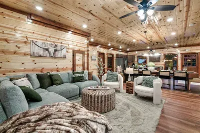 Sweeping open-concept living room with seating for the whole crew, ceiling fan overhead, and warm pine walls on every side — space that actually breathes.