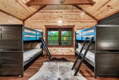 Double bunk room sleeping 6 — blue metal frames, dark accent wall, and vaulted pine ceiling. The kids' floor of the cabin, fully equipped and endlessly requested.