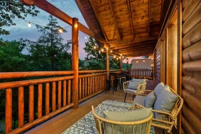 String-lit covered deck with log cabin walls and a rose-gold Smoky Mountain dusk behind the tree line — the hour after sunset belongs entirely to you out here.
