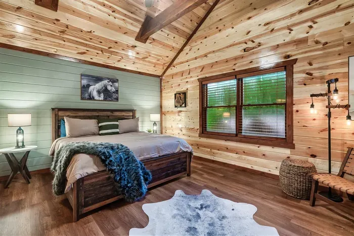 King bedroom with vaulted knotty pine ceiling, lantern sconces, and a cowhide rug underfoot — mountain lodge character with every comfort you'd expect from a premium cabin stay.