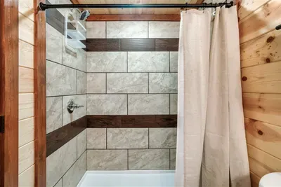 Full tiled tub and shower with warm wood surround — spotless, spacious, and stocked for the long weekend. Another bathroom that keeps up with a full house.