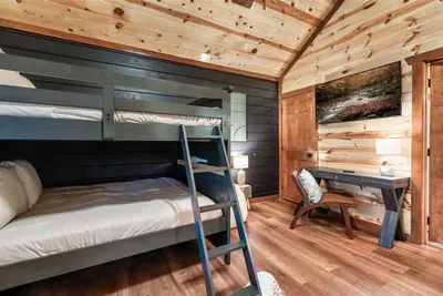 Bunk room with a reading nook, blue metal frames, and hardwood floors — kids get their own private world inside the cabin. Bedtime arguments not included.