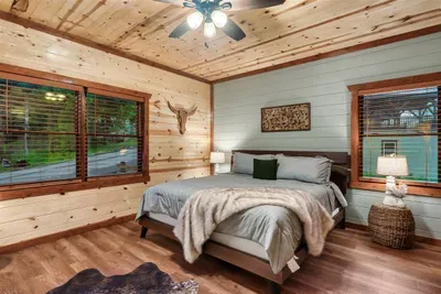 King bedroom with hardwood floors, cowhide rug, longhorn art, and a ceiling fan for warm mountain nights — Western cabin soul meets every comfort your group deserves.