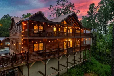Log cabin ablaze with warm light as the Smokies ignite in a crimson and amber dusk — some evenings here feel less like a vacation and more like a painting you get to live inside.