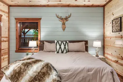 Sage-green accent wall, antler mount, and a fur-draped king bed — this bedroom balances rugged mountain soul with the softness of a genuinely restful night.