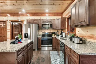 Full chef's kitchen with stainless steel appliances, granite island, and dark wood cabinetry — everything a serious home cook needs to feed the whole cabin without missing the fun.