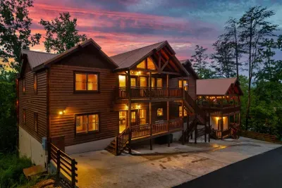 Two grand cabin buildings glowing gold against a Smoky Mountain sunset that stops you mid-sentence — this is the arrival moment your group will talk about for years.