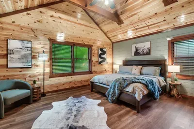 King bed under a vaulted wood ceiling, warm amber light, cowhide rug underfoot — wake up here and the whole day feels like a gift.