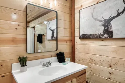 En-suite bathroom with a double vanity, oversized mirror, and a stag watching from the wall — polished mountain design where every detail was chosen with intention.