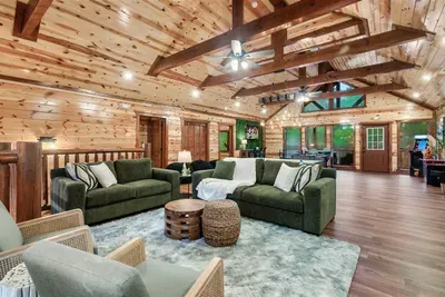Sweeping open great room with vaulted wood ceiling and oversized sectionals for the whole group — spread out, settle in, and let the cabin do its thing.