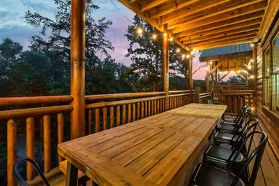 Long deck table under string lights with a violet Smoky Mountain dusk overhead — outdoor dinners here don't need a restaurant. The setting does all the work.