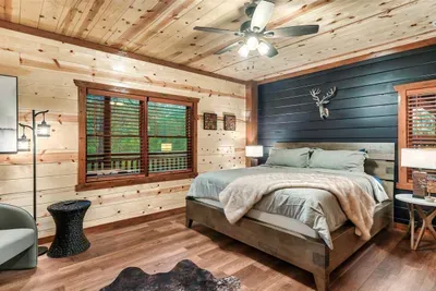 Spacious king bedroom with hardwood floors, ceiling fan, and sweeping navy walls — cool, quiet, and designed for the deep mountain sleep you've been looking forward to.